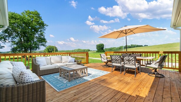 Eine Holzterrasse mit Gartenmöbeln, darunter eine Sitzecke mit Sofa, Stühlen und einem Tisch, beschattet durch einen großen Sonnenschirm.