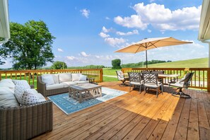 Une terrasse en bois, aménagée avec du mobilier d’extérieur, notamment un canapé, des fauteuils et une table, le tout placé sous un grand parasol.