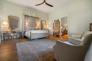 Quarto com cama, escrivaninha, cadeira, espelho grande e ventoinha no teto.