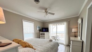 Une chambre à coucher comprenant un lit, un ventilateur de plafond, un téléviseur et une vue sur l’extérieur grâce à une porte coulissante.