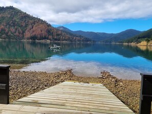 Um píer de madeira que se estende por um lago calmo, com um barco, rodeado por colinas arborizadas.