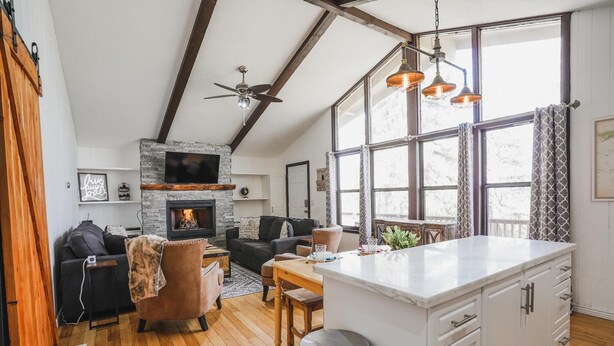 A modern living room with a fireplace, wooden floors, a dining area, and large windows. - Pet friendly/walk to restaurant/bar and golf  (Flagstaff)