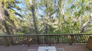 A covered outdoor deck with a table and chairs, surrounded by a wooden railing and trees. - Pet friendly/walk to restaurant/bar and golf  (Flagstaff)