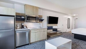 Una habitación de hotel moderna con kitchenette, televisión de pantalla plana, cama y una mesa de centro blanca.