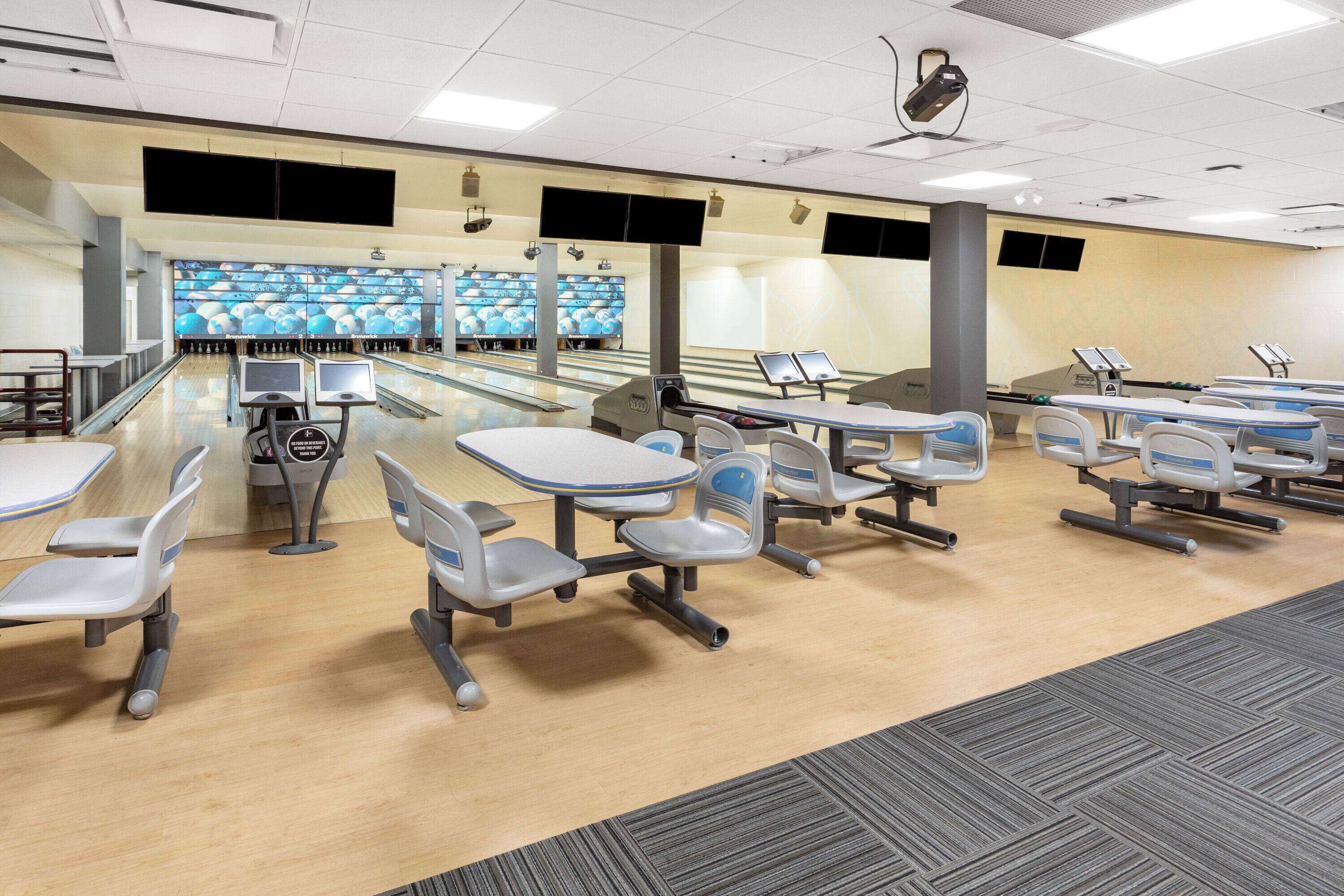 A bowling alley with multiple lanes, seating areas, and a large screen displaying bowling games.