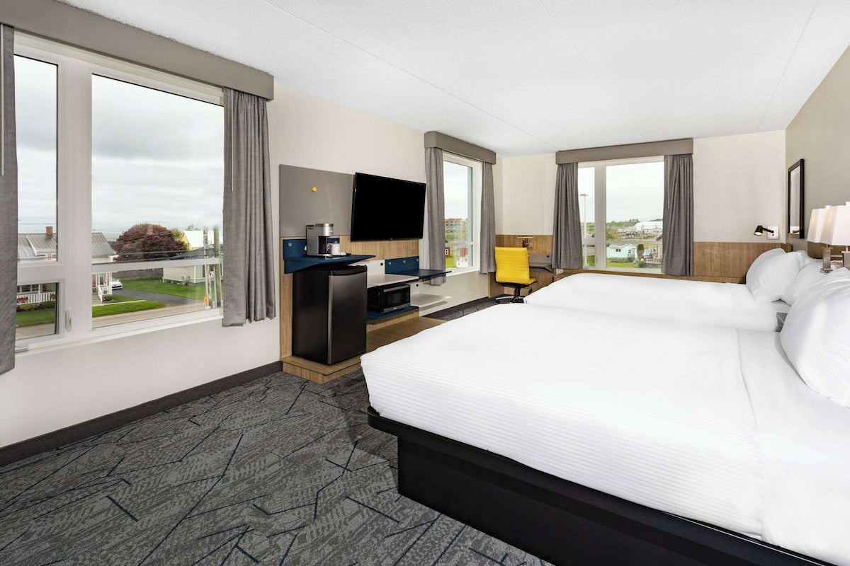 Et hotelværelse med en stor seng, et fjernsyn, et skrivebord med en computer og udsigt ud.