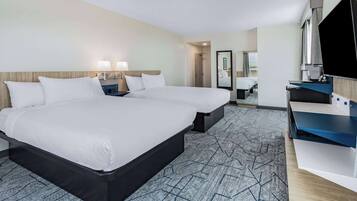 A hotel room with a large bed, a desk with a flat-screen TV, and a shower area.