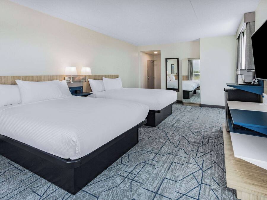 A hotel room with a large bed, a desk with a flat-screen TV, and a shower area.