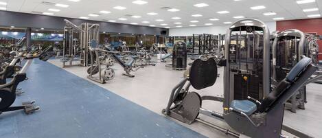 A gym with various exercise machines, a blue floor, and a mirrored wall.