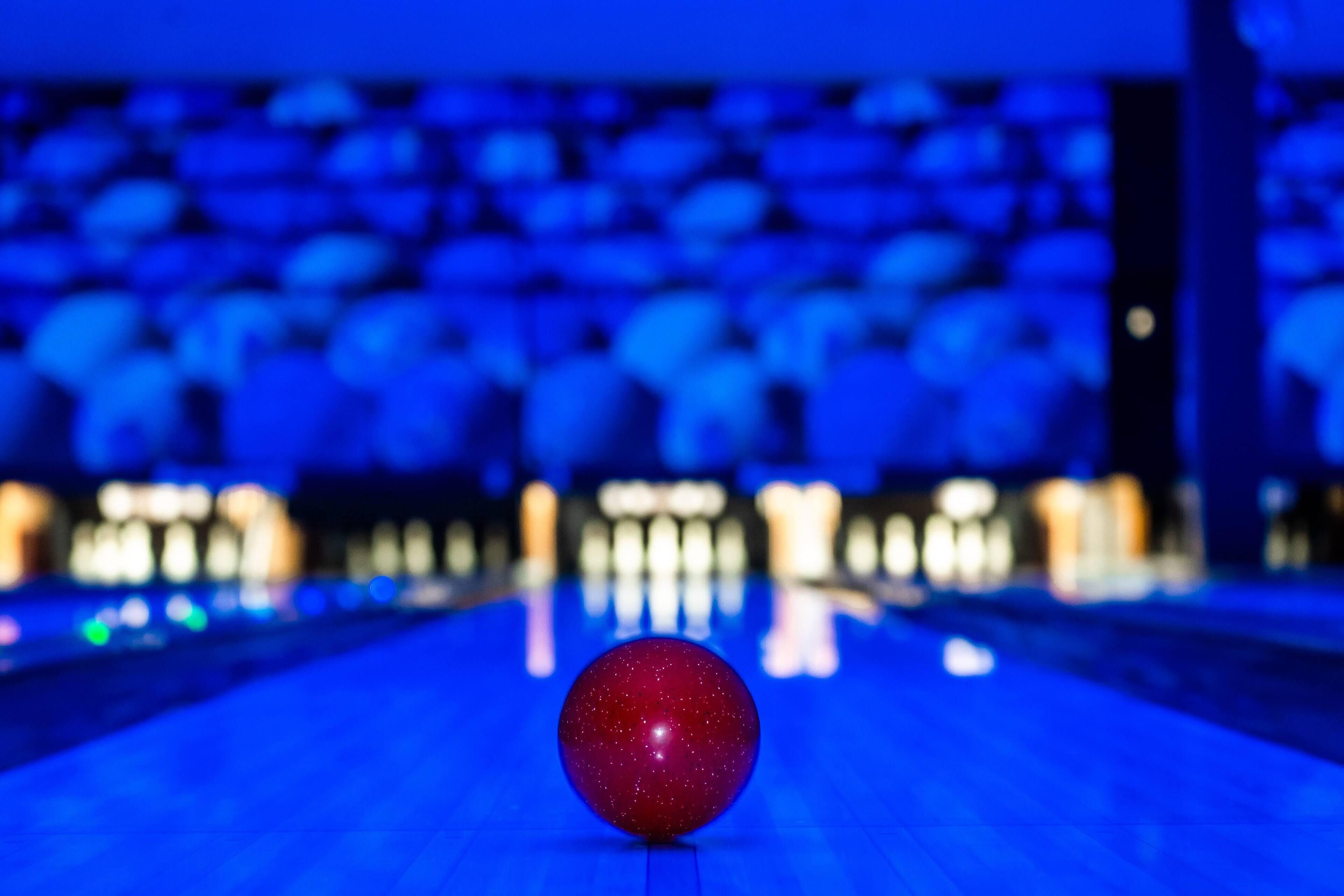 Ein roter Bowlingball auf der Bahn, im Hintergrund verschwommene Lichter.
