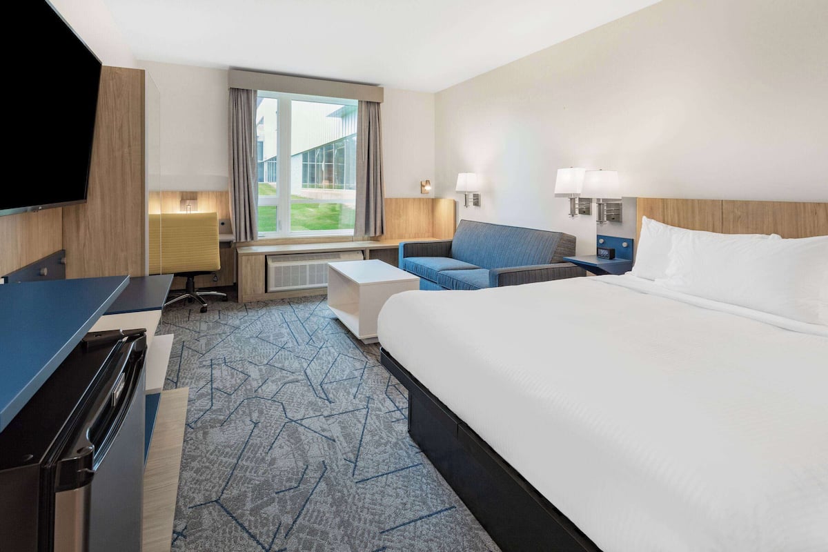 Et hotelværelse med en stor seng, et skrivebord med computer, en stol og et fjernsyn.