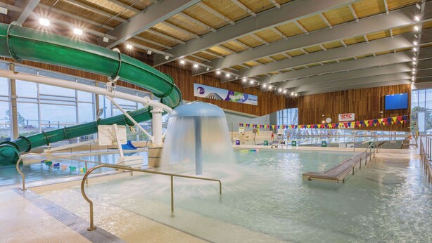 Una piscina interior con tobogán de agua, zona de vestuarios y bar.