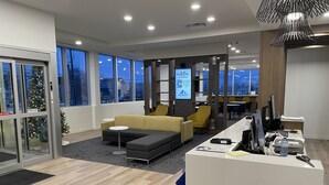 Un moderno vestíbulo de hotel con mostrador de recepción, zona de estar y amplios ventanales con vistas a la ciudad.