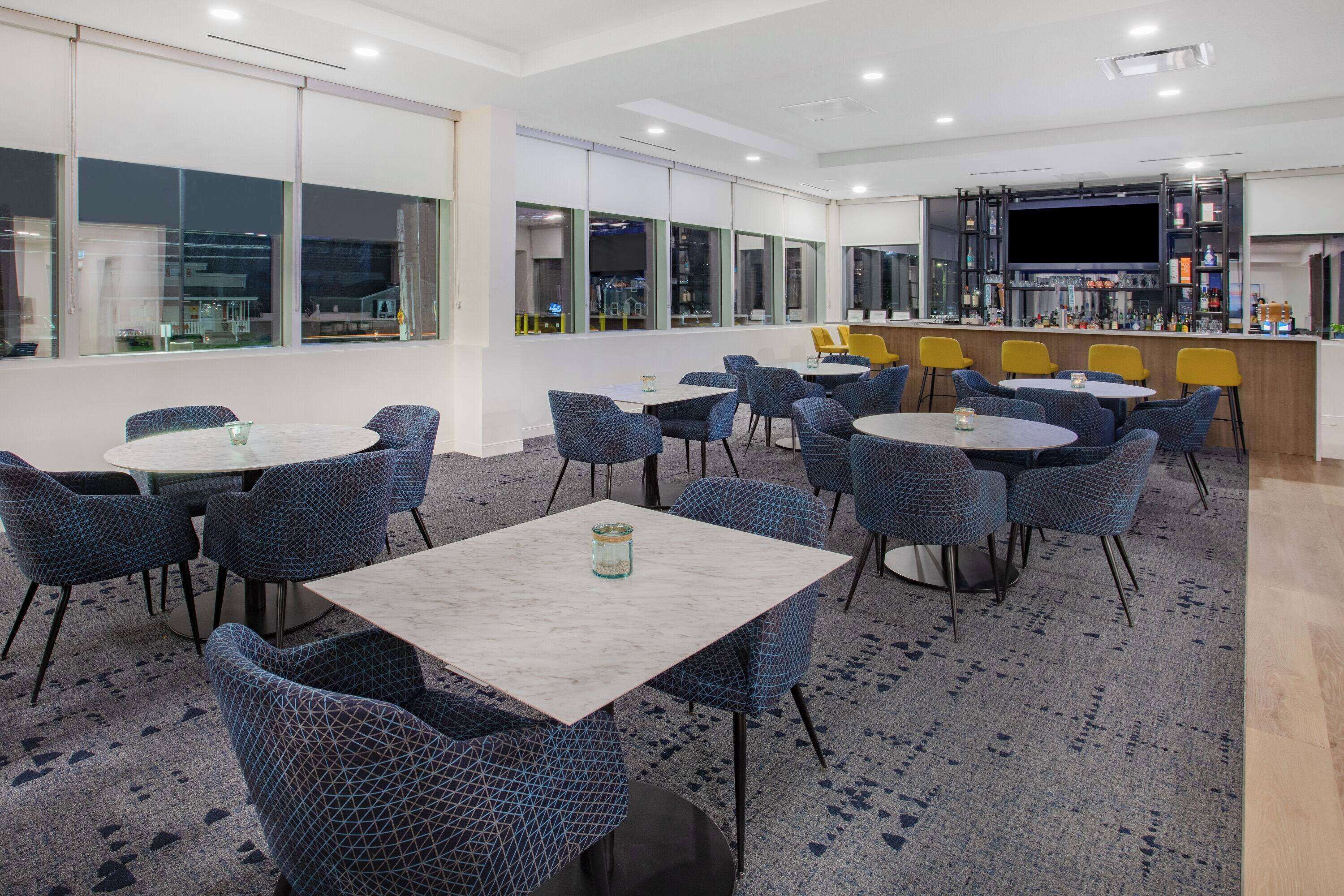A modern conference room with round tables and chairs, a large TV screen, and a bar area.
