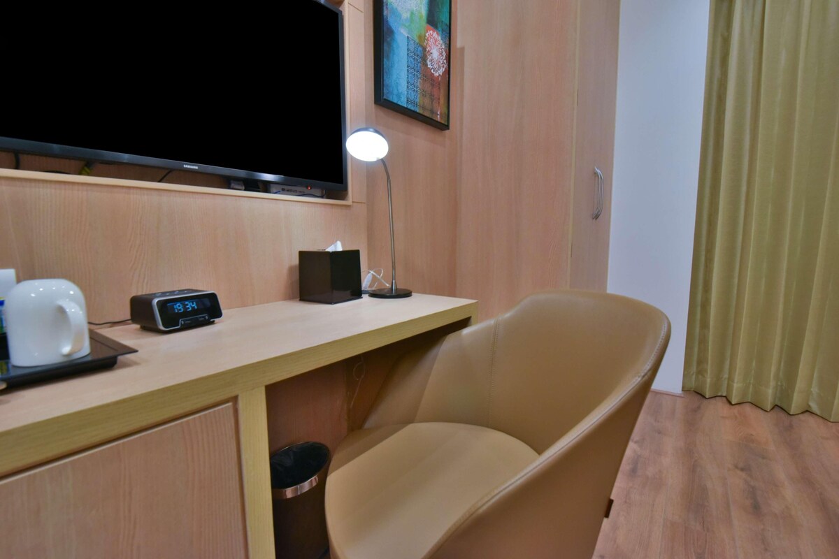 Une chambre d’hôtel avec un bureau en bois, une télévision, une lampe, une chaise et une poubelle.