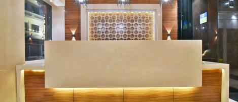 A reception desk with a wooden panel design, three pendant lights, and a glass partition with a geometric pattern.