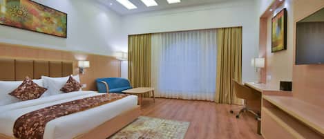 A hotel room with a large bed, a desk, a chair, a TV, and a window with curtains.