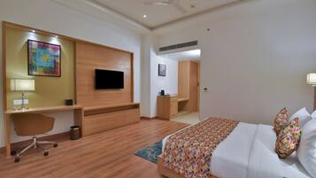 Una habitación de hotel moderna con piso de madera, una cama con ropa de cama estampada, un escritorio con silla, un televisor montado en la pared y un armario.