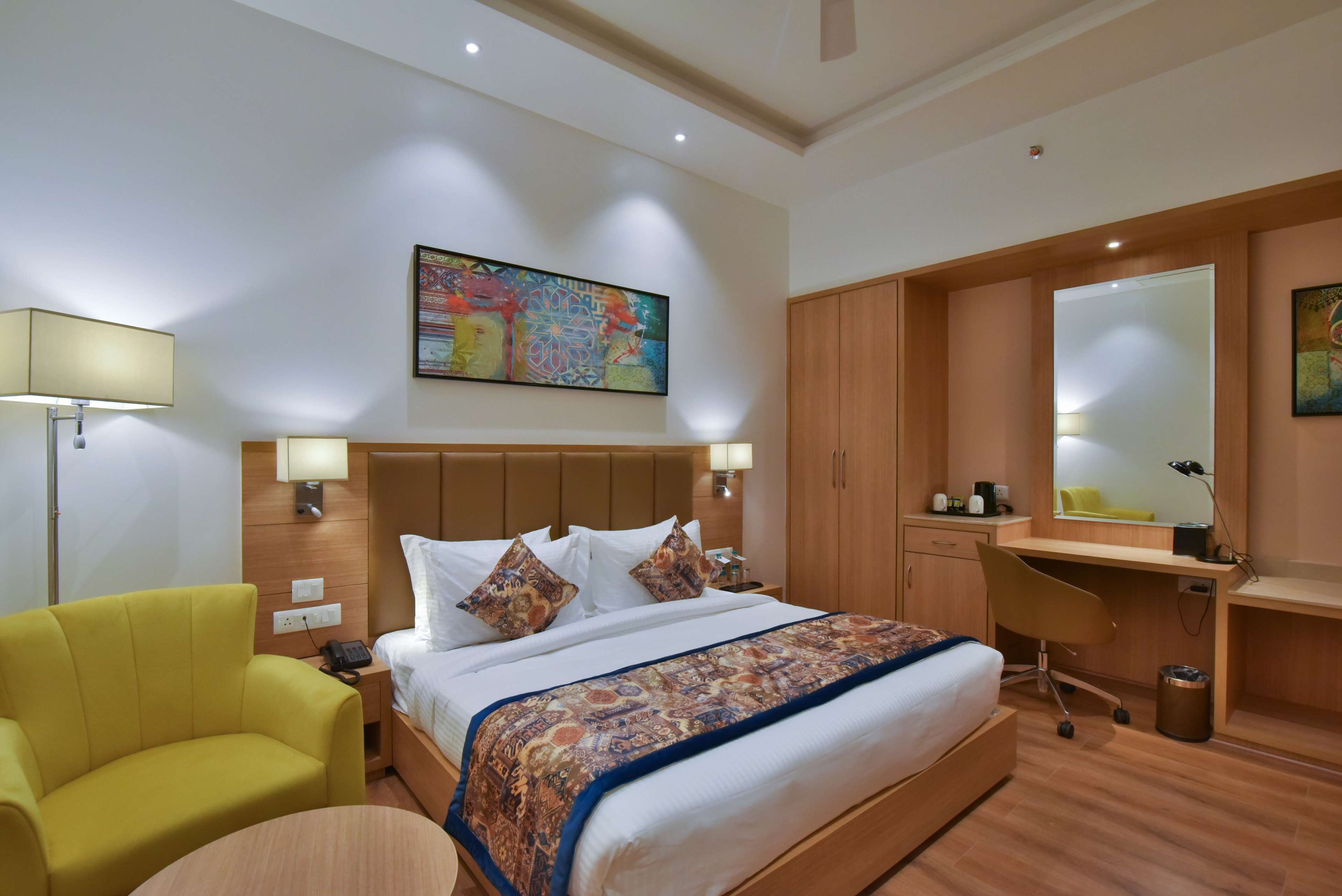 A hotel room with a large bed, a desk, a chair, and a lamp.