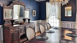 Une salle à manger avec une table en bois, des chaises, un lustre et un grand miroir.