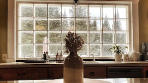 Une cuisine dotée d’une grande fenêtre, d’un plan de travail rond en marbre et d’un vase contenant des fleurs séchées.
