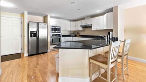 A modern kitchen with white cabinets, stainless steel appliances, and a central island with bar stools.