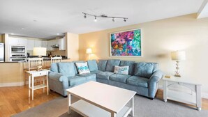 A living room with a light blue sofa, a white coffee table, and a colorful abstract painting on the wall.