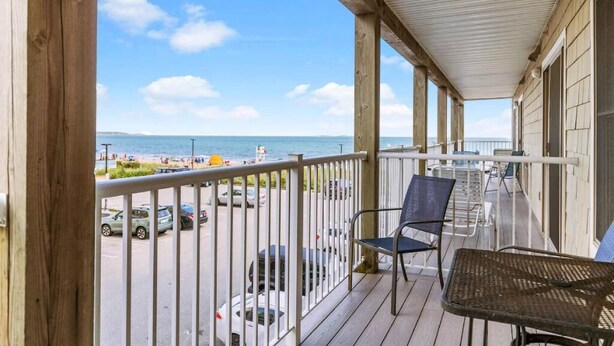 A wooden deck with a view of the beach and ocean, featuring two chairs and a table.