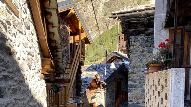 A narrow cobblestone street flanked by stone buildings with wooden balconies and a mountain backdrop. - Entire Chalet with fireplace. garden, Wi-Fi, adjacent to village center (Paquier)