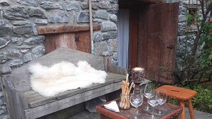 A rustic outdoor seating area with a stone wall, wooden benches, and a fur-covered bench. - Entire Chalet with fireplace. garden, Wi-Fi, adjacent to village center (Paquier)