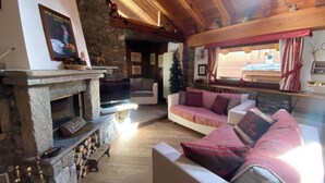 A cozy living room with a stone fireplace, a sofa, and a television. - Entire Chalet with fireplace. garden, Wi-Fi, adjacent to village center (Paquier)