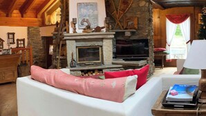 A cozy living room with a stone fireplace, a white sofa with pink cushions, and a wooden ceiling. - Entire Chalet with fireplace. garden, Wi-Fi, adjacent to village center (Paquier)