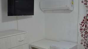 Ein kleiner, sauberer Raum mit Bett, Schreibtisch, Fernseher, Minikühlschrank und Kleiderschrank.