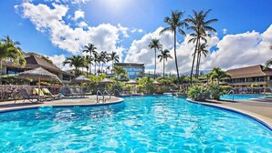 Ein Pool mit Liegestühlen und Palmen, umgeben von Hotelgebäuden.