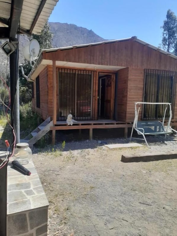 A wooden cabin with a porch, a dog sitting on the porch, and a chair.