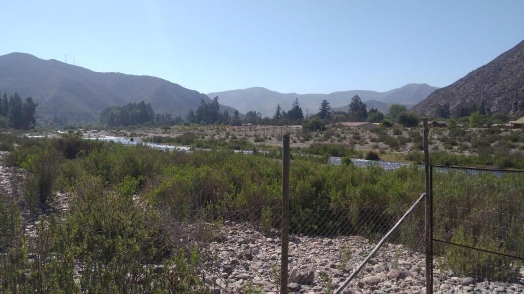 Paisaje natural con río, montañas y un área cercada.