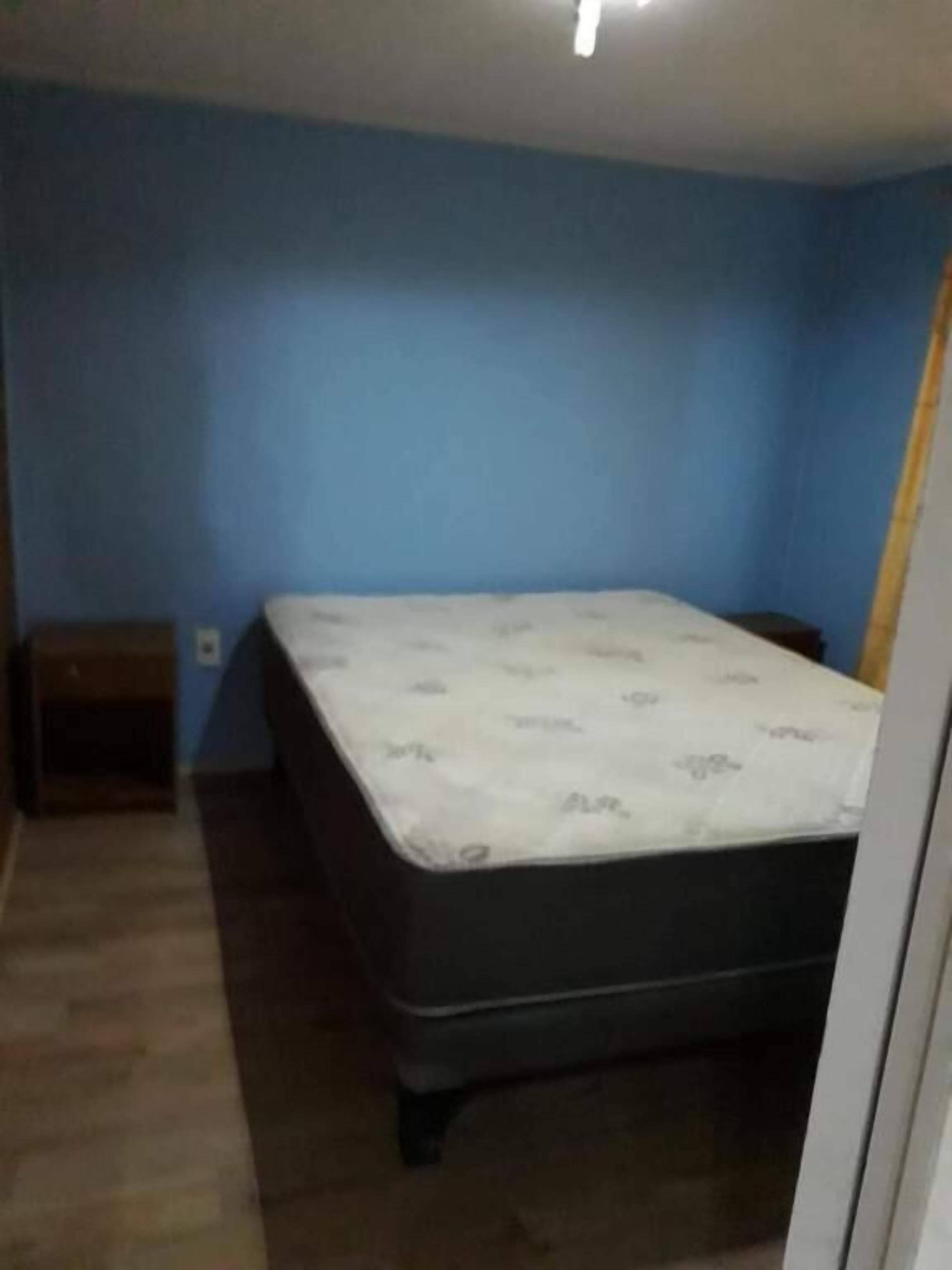 Un dormitorio con una cama individual, una mesita de noche y una pared azul.