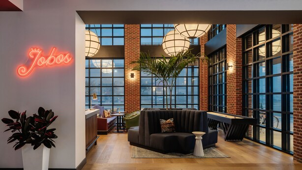 A modern lounge area with a neon sign, large windows, and a pool table.