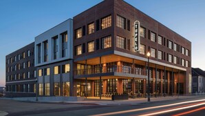 A modern hotel with a brick facade, large windows, and a covered outdoor seating area.