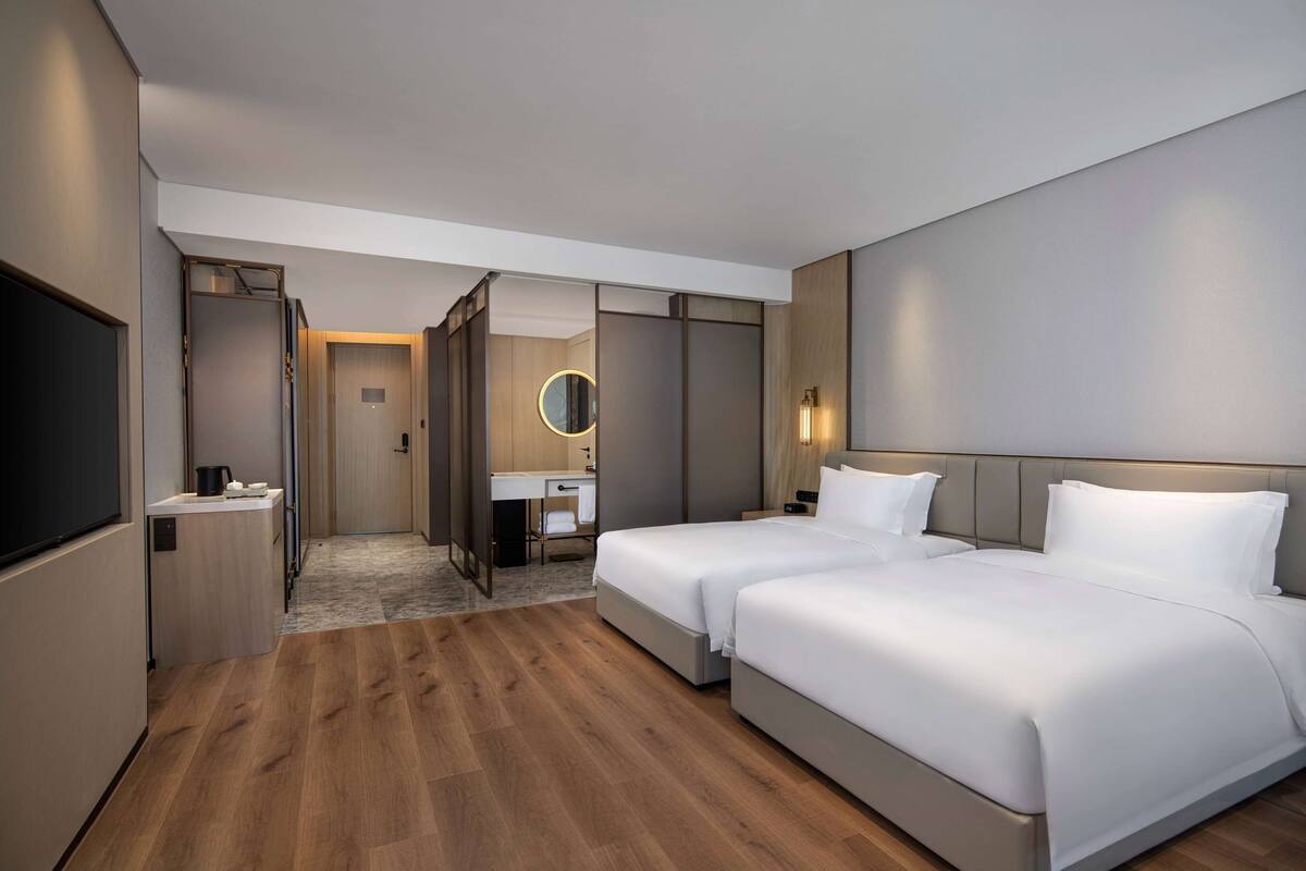 Habitació d'hotel amb dos llits, un escriptori, un mirall i un televisor.