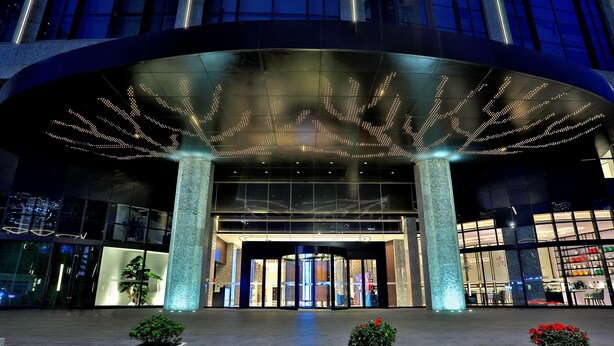 A modern hotel entrance with a curved glass facade, illuminated signage, and a central entrance with automatic doors. - Wyndham Garden Hangzhou Yuhang (Hangzhou)