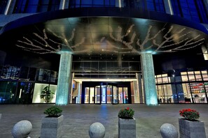 En moderne hotelindgang med en buet glasfacade, oplyste skilte og en central indgang med automatiske døre.