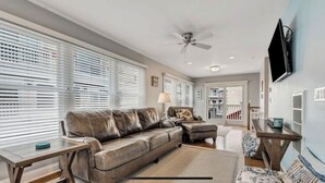 A living room with a leather sofa, a coffee table, a TV mounted on the wall, and a ceiling fan. - Beautiful New Spacious Townhome w/ Pool, Steps to Beach/Boardwalk, 3 Levels (Seaside Heights)