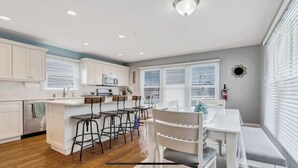 A modern kitchen with white cabinets, a central island with bar stools, and a dining area with a bench. - Beautiful New Spacious Townhome w/ Pool, Steps to Beach/Boardwalk, 3 Levels (Seaside Heights)