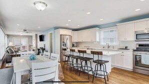 A modern kitchen with white cabinets, a central island with bar stools, and a built-in oven. - Beautiful New Spacious Townhome w/ Pool, Steps to Beach/Boardwalk, 3 Levels (Seaside Heights)