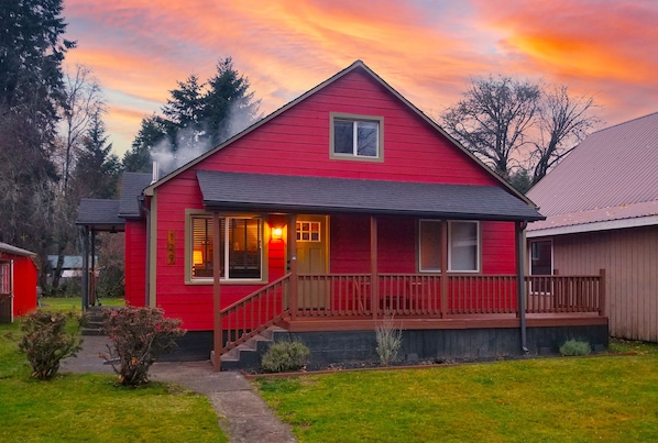 A red house with a porch and a chimney emitting smoke.