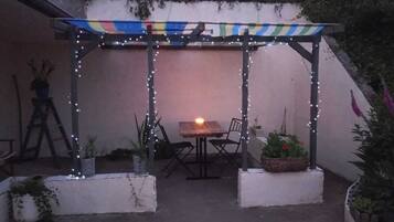 A covered patio area with a table and chairs, string lights, and potted plants.