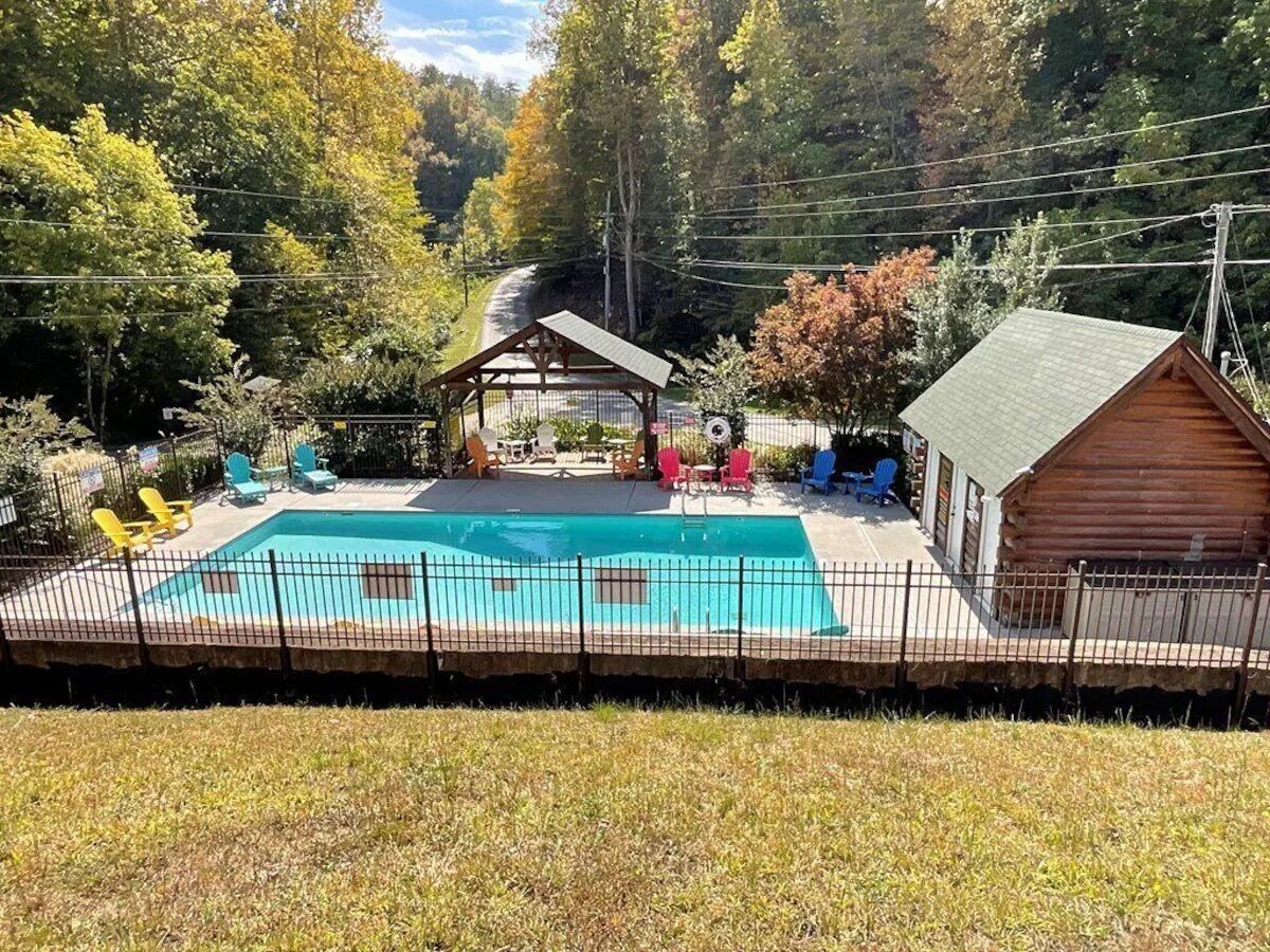 A swimming pool with a fenced deck, a covered seating area, and a wooden cabin.