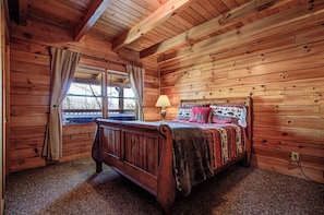 Quarto de cabana de madeira com cama, janela com cortinas e uma luminária.
