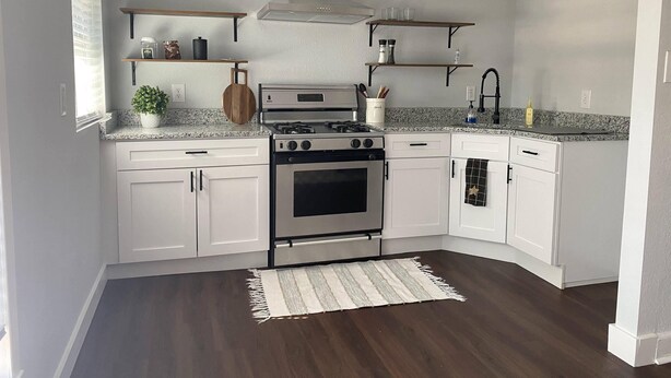 Una cocina moderna con armarios blancos, una estufa de acero inoxidable y estanterías de madera.
